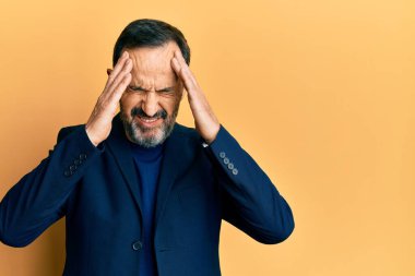Orta yaşlı İspanyol bir adam iş kıyafetleri giyiyor, elleri kafasında, stresten baş ağrısı çekiyor. migren ağrısı. 
