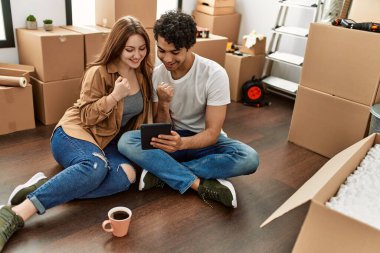 Genç çift mutlu bir şekilde dokunmatik ped kullanıyor ve yeni evlerinde kahve içiyor..