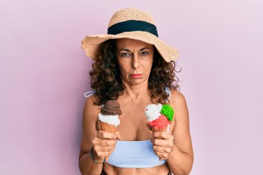Orta yaşlı İspanyol kadın yaz tarzı giyiniyor. Elinde dondurmacı kuşkusu ve gerginliği var. Sorunları yüzünden surat asıyor. negatif kişi. 