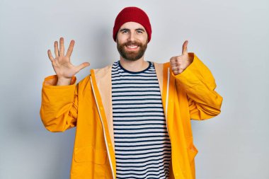 Sakallı, sarı yağmurluklu beyaz bir adam altı numaralı parmaklarıyla gülümseyerek, kendinden emin ve mutlu görünüyor.. 