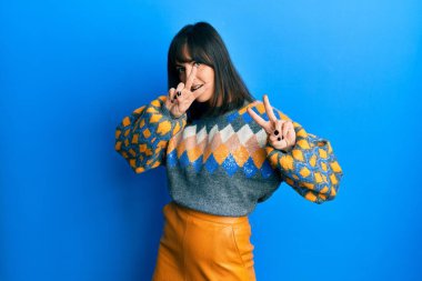 Günlük kazak giyen genç İspanyol kadın kameraya bakıp zafer işareti yaparken gülümsüyor. İki numara.. 