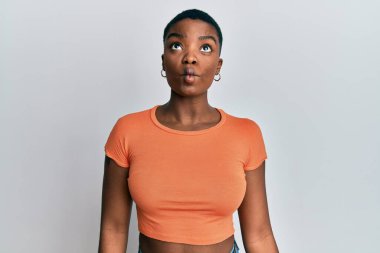 Günlük turuncu tişört giyen genç Afro-Amerikan kadın dudaklarıyla balık suratı yapıyor, çılgınca ve komik bir jest. Komik ifade. 