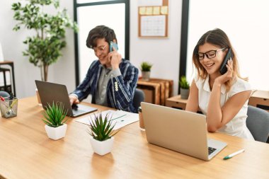 Ofiste akıllı telefon ve dizüstü bilgisayarla çalışırken gülümseyen iki iş adamı..