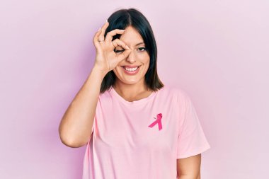 Tişörtüne pembe kanser kurdelesi takmış genç İspanyol kadın el hareketleriyle gülümsüyor ve mutlu yüzüyle parmaklarının arasından bakıyor.. 