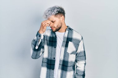 Modern boyalı saçlı, gündelik gömlek giyen, burnu ve gözleri ovuşturmaktan yorgun, yorgun ve baş ağrısı çeken genç İspanyol bir adam. Stres ve hüsran kavramı. 