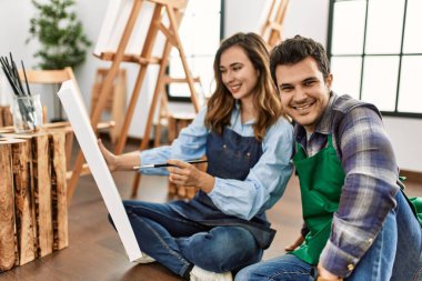 Resim yaparken gülümseyen iki öğrenci sanat okulunda yerde oturuyor..