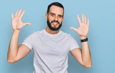 Sakallı, günlük beyaz tişörtlü, on numarayı gösteren ve gülümseyen, kendinden emin ve mutlu bir genç.. 