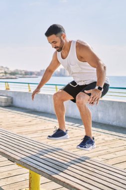 İspanyol bir adam güneşli bir günde bankta zıplayarak spor yapıyor.