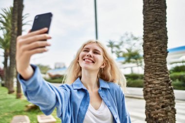 Genç sarışın kadın güneşli bir günde akıllı telefonuyla selfie çekiyor.