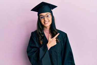 Mezuniyet şapkası ve tören cübbesi giyen genç İspanyol kadın. Yüzünde mutlu ve doğal bir ifadeyle elleri ve parmaklarıyla gülümseyen bir gülümseme. 