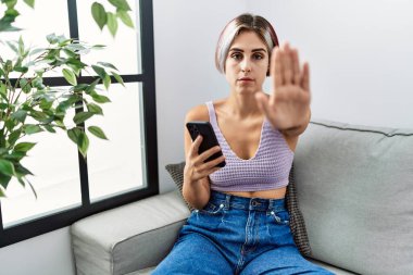 Genç ve güzel bir kadın koltukta oturmuş akıllı telefon mesajı yazarak şarkı söylemeyi kesiyor. Yüzünde olumsuz ve ciddi bir jest olan uyarı ifadesi. 