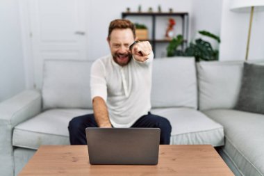 Orta yaşlı bir adam evde dizüstü bilgisayar kullanıyor. Kameraya kızgın ve sinirli. Sana kızgın. 