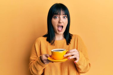 Genç İspanyol kadın elinde kahveyle çılgınca kutlama yapıyor ve başarıya hayret ediyor gözleri açık heyecanla haykırıyor. 