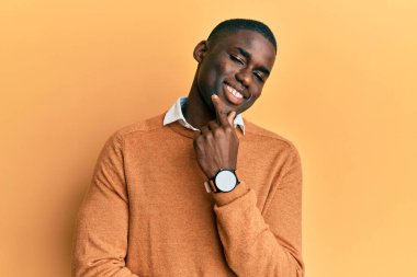 Gündelik giysiler giymiş genç Afro-Amerikan adam kameraya kendinden emin bakıyor kollarını kavuşturmuş ve çenesini kaldırmış bir şekilde gülümsüyor. Olumlu düşünmek. 