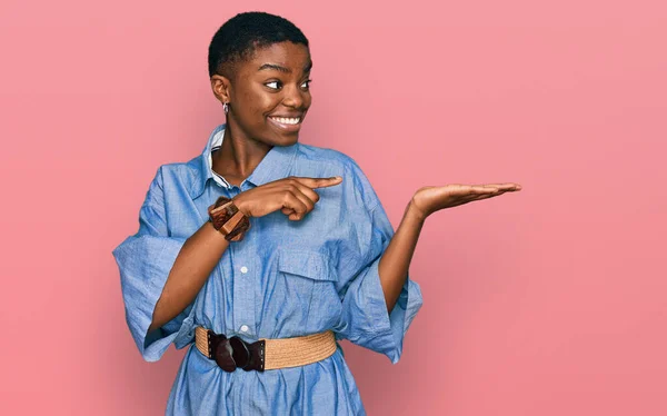 手で提示し 指で指している間若いアフリカ系アメリカ人の女性は カジュアルな服を着てカメラに驚いて笑顔 — ストック写真
