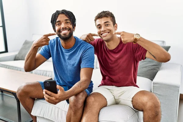 Hombres Hispanos Jóvenes Usando Teléfono Inteligente Sentado Sofá Casa Sonriendo —  Fotos de Stock