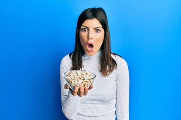 Young Hispanic Woman Holding Pumpkin Seeds Bowl Scared Amazed Open — Stock Photo, Image