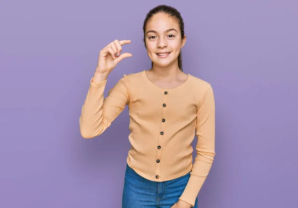 美しいブルネットの女の子は カジュアルなセーターを着て笑顔と指を見て カメラで小さなサイズの看板を行う手で自信を持ってジェスチャー 概念を測定し — ストック写真