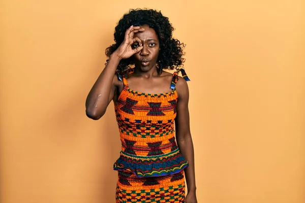 アフリカの伝統的な服を着ている若いアフリカ系アメリカ人女性は 驚くべき顔でショックを受け 目は指を通して見ている 信じられない表現 — ストック写真