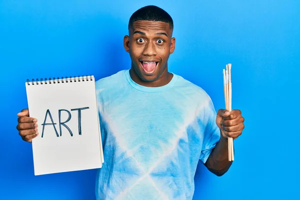 Joven Negro Sosteniendo Cuaderno Arte Pinceles Pintor Celebrando Loco Sorprendido — Foto de Stock