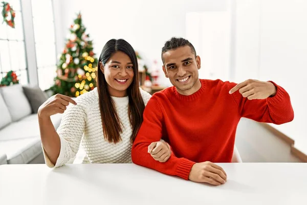 Young Latin Couple Sitting Table Christmas Tree Looking Confident Smile — Zdjęcie stockowe