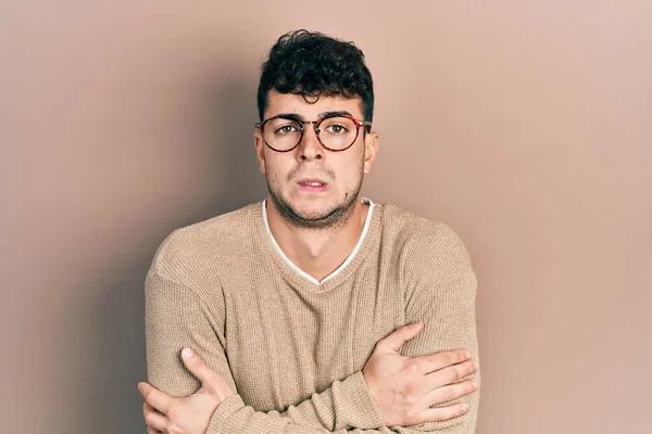 Young hispanic man wearing casual clothes and glasses shaking and freezing for winter cold with sad and shock expression on face