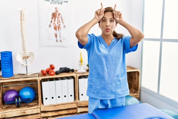 Orta yaşlı İspanyol fizyoterapist kadın ağrı kesici kliniğinde çalışıyor. Parmağını boynuzlarına geçirip komik jestler yapıyor. 