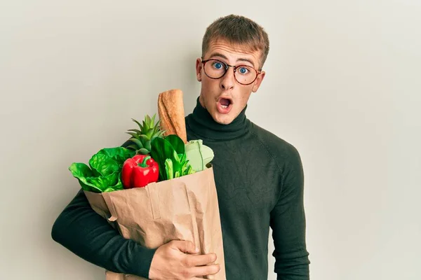 年轻的高加索人拿着装有食品杂货的纸袋 惊慌失措 张大了嘴 满脸诧异 — 图库照片