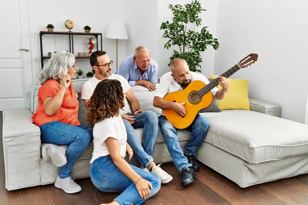 Group of middle age friends having party playing classical guitar sitting on the sofa at home.