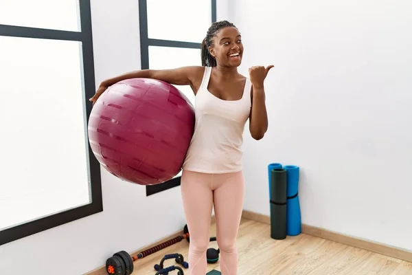 Ung Afrikansk Amerikansk Kvinna Med Flätor Håller Pilatesboll Yogarummet Pekar — Stockfoto