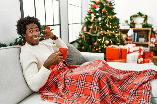 Hombre Afroamericano Joven Sentado Sofá Bebiendo Café Por Árbol Navidad — Foto de Stock