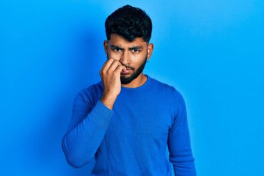 Sakallı, sıradan mavi süveter giyen, gergin ve elleri ağızdan tırnak yiyen bir Arap. anksiyete. 