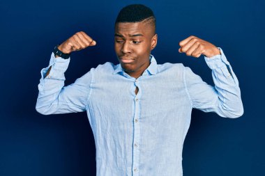 Sıradan kıyafetler giyen genç Afrikalı Amerikalı gururla gülümseyen kol kaslarını gösteriyor. fitness konsepti. 