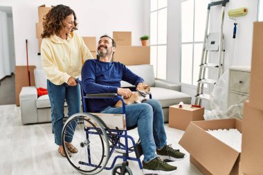 Orta yaşlı İspanyol çift mutlu gülümsüyor. Tekerlekli sandalyede oturan bir adam ve yeni evinde ayakları üzerinde duran bir köpek.