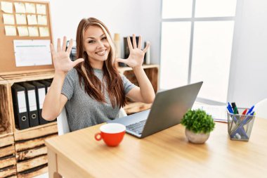 Ofiste çalışan genç esmer kadın dizüstü bilgisayarı ile on numarayı gösterip işaret ederken kendinden emin ve mutlu bir şekilde gülümsüyor.. 