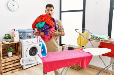 Çamaşırları ütülemeye hazır genç yakışıklı bir adam. Korkmuş ve şaşkın bir şekilde ağzı açık, şaşırmış, inançsız bir yüz. 