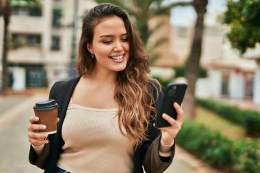 Genç İspanyol kadın akıllı telefon kullanıyor ve şehirde kahve içiyor..