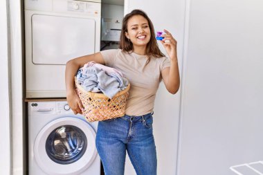 Çamaşır sepetinde çamaşır ve deterjan taşıyan İspanyol bir kız.