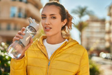 Gevşek yüzlü genç İspanyol kız şehirde bir şişe su içiyor..