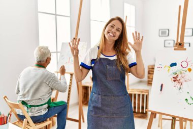 Resim stüdyosunda önlük giyen İspanyol kadın dokuz numarayı gösterip işaret ederken kendine güvenen ve mutlu bir şekilde gülümsüyor.. 