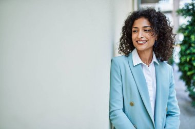 Profesyonel giyinen genç İspanyol iş kadını. Şehre gülümsüyor. Duvara yaslanıyor.