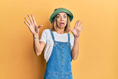 Kot pantolon ve 90 'ların tarzında şapkalı beyaz kadın korku ifadesinden korkuyor ve dehşete düşüyor. El hareketlerini durdur, şok içinde bağır. panik konsepti. 