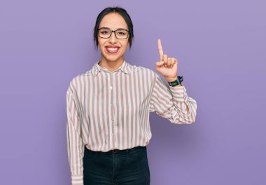 Gündelik kıyafetler giyen ve gözlüklü genç İspanyol kız bir numarayı gösterip işaret ederken kendinden emin ve mutlu bir şekilde gülümsüyor.. 