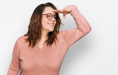 Gündelik kıyafetler ve gözlük takan genç ve cüsseli bir kadın çok mutlu ve gülümseyerek başını kaldırıp uzaklara bakıyor. arama kavramı. 