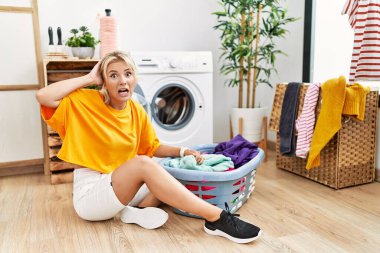 Kirli çamaşırları çamaşır makinesine koyan beyaz bir kadın elleri başının üstünde korkmuş ve ağzı açık bir şekilde şok geçirmekten korkan genç bir kadın. 