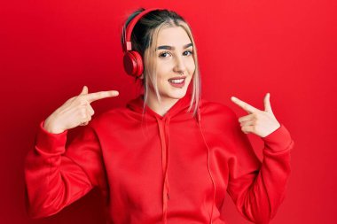 Genç, modern bir kız spor kıyafetleri giyiyor ve kulaklık takıyor. Gülümsüyor, parmaklarıyla ve ağzıyla gülümsüyor. diş sağlığı kavramı. 