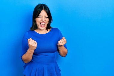 Gündelik kıyafetler giyen genç İspanyol kadın başarı için heyecanlı kolları havada ve gözleri kapalı zaferi kutlarken gülümsüyor. Kazanan konsept. 