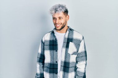 Modern boyalı saçlı, sıradan gömlekli, yüzünde gülümseme ve doğal ifadeyle yan yana bakan İspanyol bir genç. Kendinden emin gülen. 