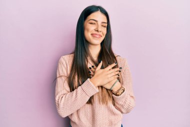Gündelik kıyafetler giyen genç İspanyol kadın elleri göğsünde gülümsüyor, gözleri kapalı, yüzünde minnet ifadesi var. sağlık kavramı. 