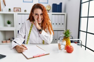 Klinikteki genç kızıl saçlı kadın beslenme uzmanı el üstünde gizli dedikodular söylüyor, kötü niyetli konuşmalar fısıldıyor. 
